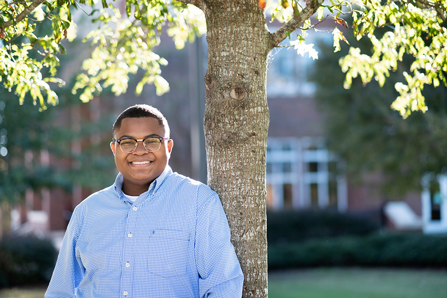 Christopher Robinson smiles while leaning next to a tree.