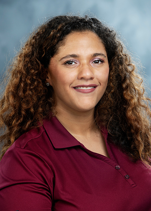 Studio portrait of Christien Russell wearing a maroon shirt, in front of blue backdrop