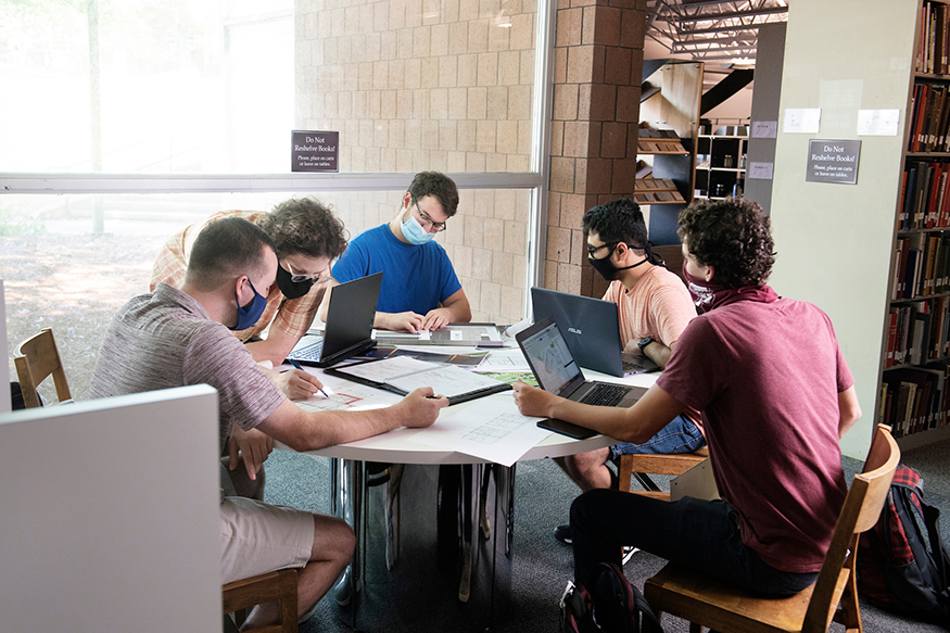 Five young men work on computers around a table.