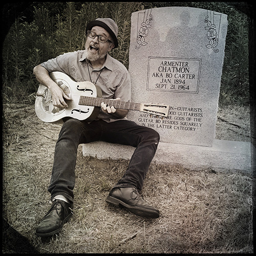 Blues musician Steve Cheseborough sings and plays a Bo Carter song on his guitar while sitting at Carter’s grave marker in Nitta Yuma, Mississippi. Cheseborough is among the world-renowned musicians who are bringing their talents to Mississippi State University Libraries’ 12th annual Templeton Ragtime and Jazz Festival March 22-24. (Photo submitted/courtesy of Bill Steber)