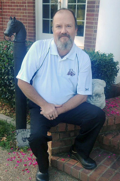 Herbert Strickland sits next to a Bulldog statue and "Bulldog Crossing" sign on his front porch.