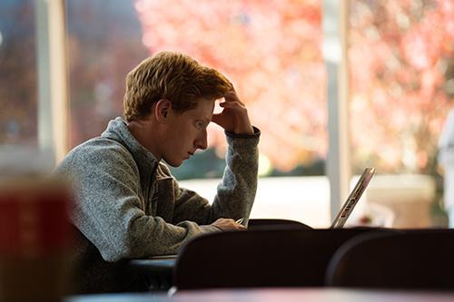 A male student looks at his laptop in the atrium of McCool Hall.