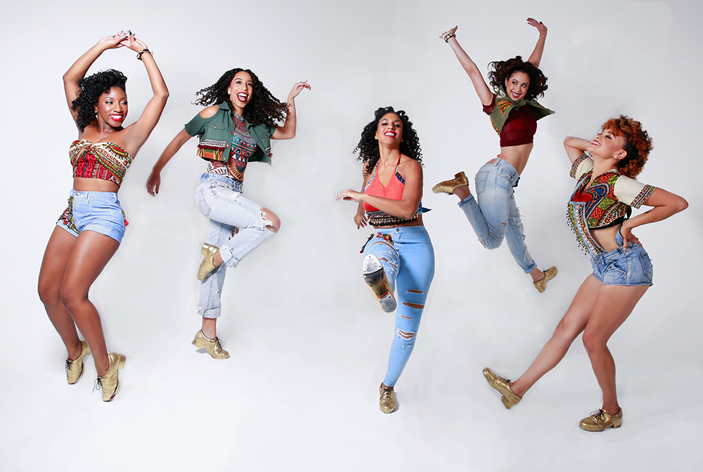Members of Syncopated Ladies tap dance band jump in front of a white background.