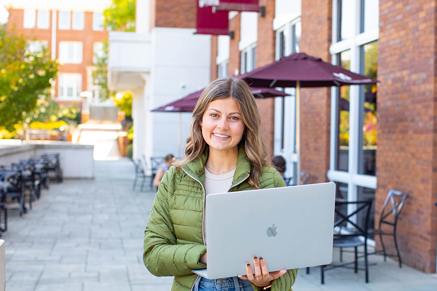 A student holds a laptop while outside on the MSU campus.