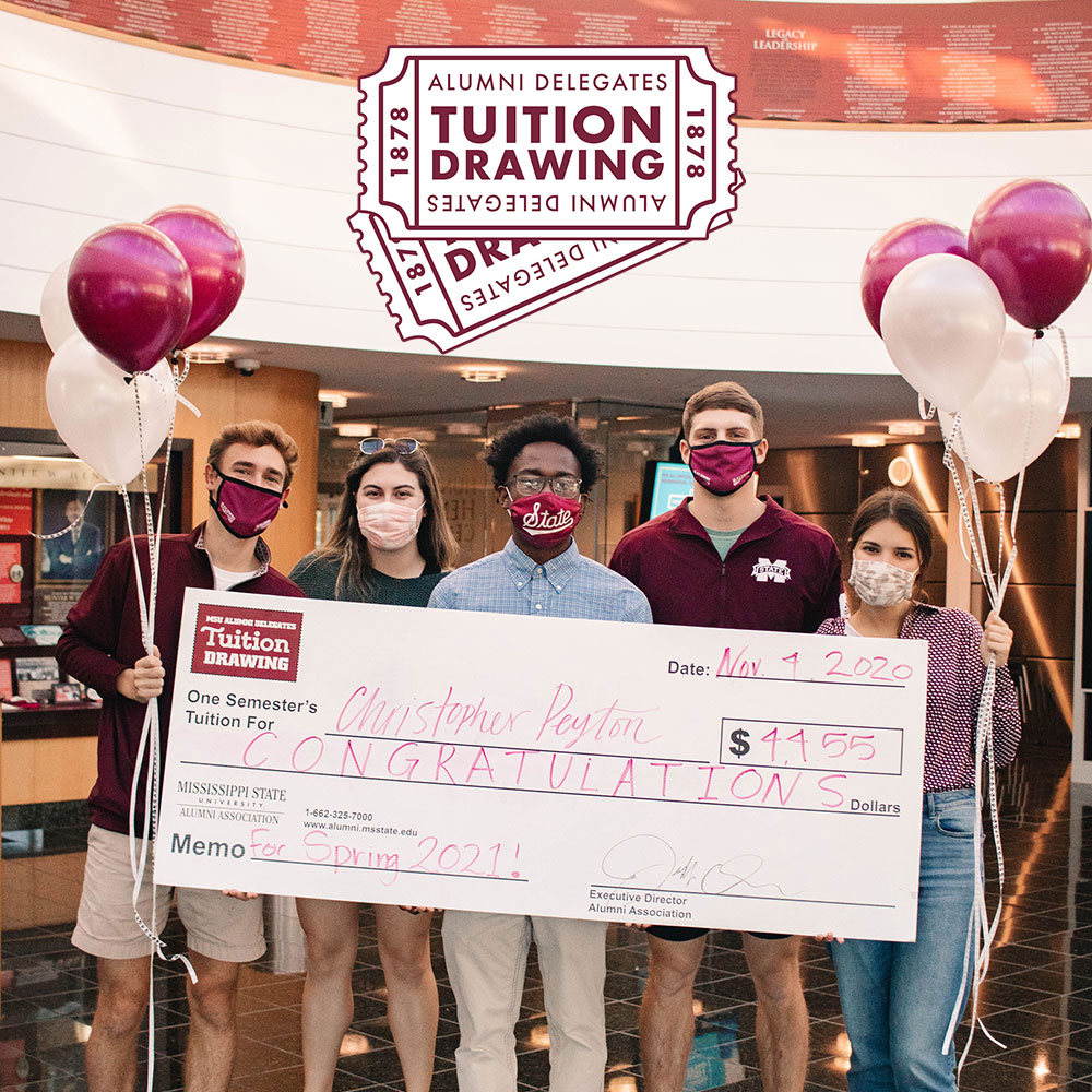 Members of the MSU Alumni Delegates hold maroon and white balloons while presenting MSU student Christopher Peyton with a check for a free semester of tuition.