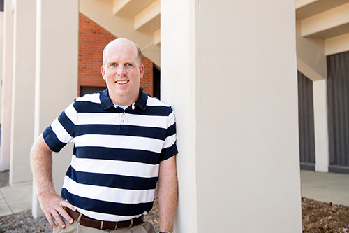 Greggory J. Twietmeyer pictured wearing a blue and white striped shirt standing near a concrete post