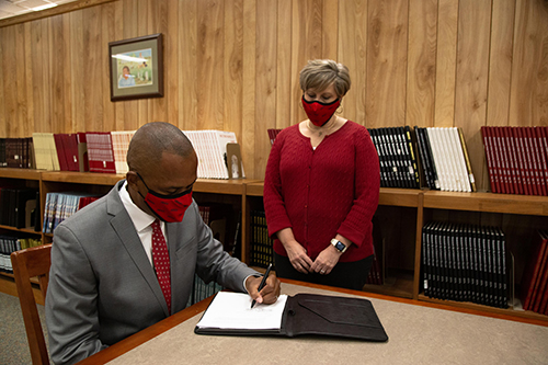 MDCC President Tyrone Jackson is pictured seated at a large table while Kristy Bariola, Mississippi Delta Community College Director of Library Services stand behind him in front of a large display of library books.