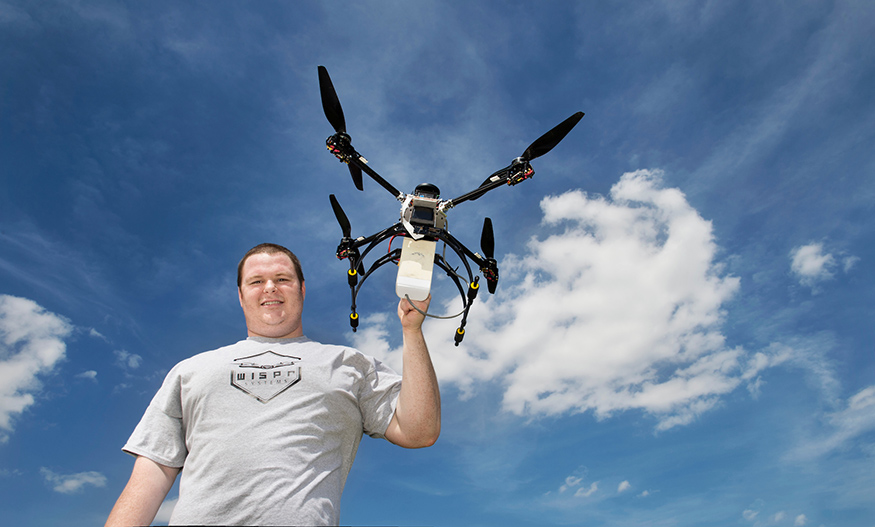 Conor Ferguson stands holding a drone with the blue sky in the background.