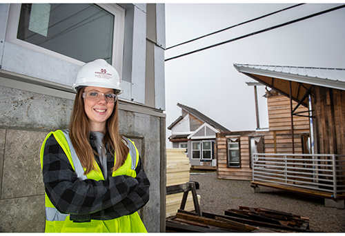 Jalyn Wallin wearing a construction vest and hat while standing near a house