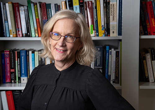 MSU Assistant Professor Carol Cutler White smiles while standing on front of shelves full of colorful books.