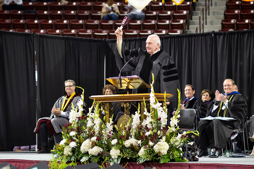 Former Rhode Island Supreme Court Chief Justice Frank J. Williams rings a cowbell before addressing Mississippi State’s approximately 3,200 spring graduates in Humphrey Coliseum. (Photo by Robert Lewis)