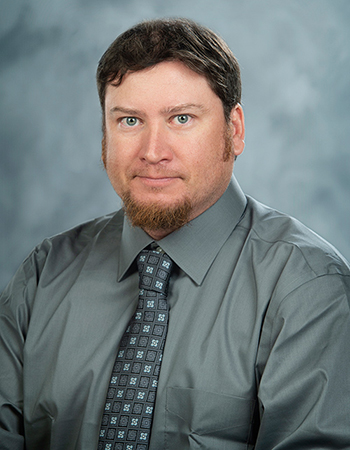 Portrait of Jon Woody, he is wearing a gray shirt and blue patterned tie