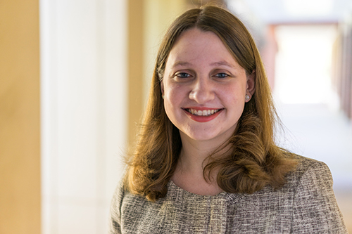 Stephanie Freeman smiles for the camera while standing in a brightly-lit room with a doorway in the distance.