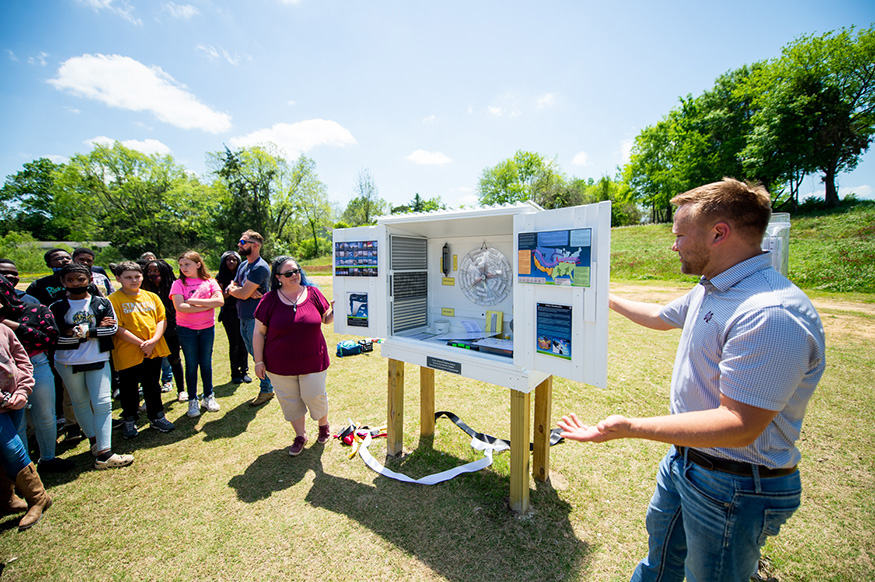 Two MSU faculty members demonstrate a weather station in front of Partnership Middle School students.