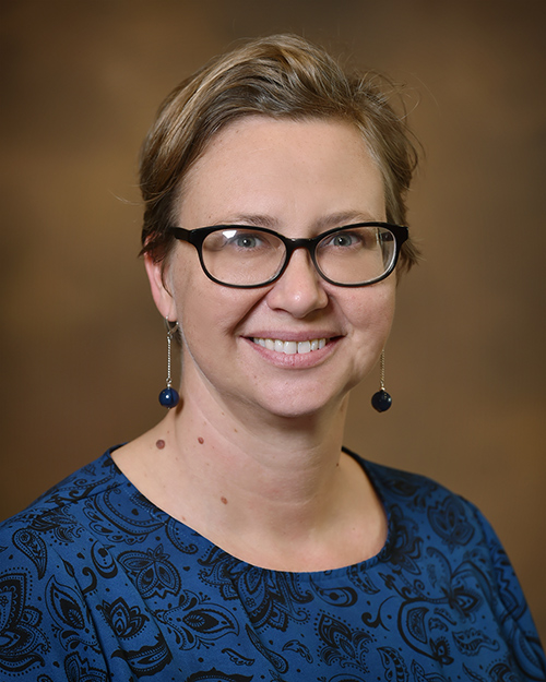 Portrait of Jennifer Courts wearing glasses in front of a tan backdrop