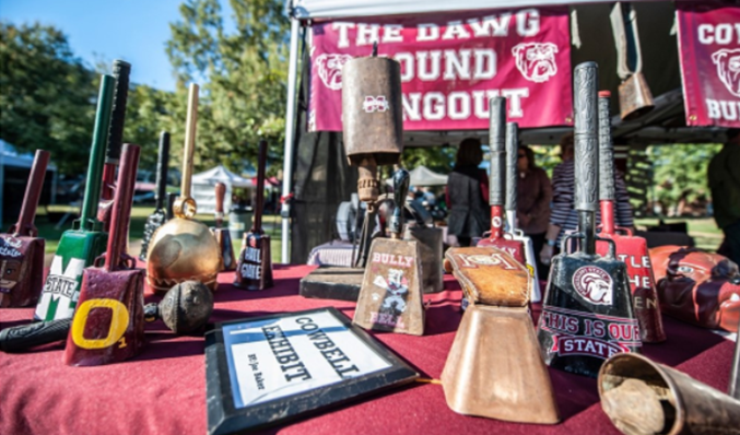 An assortment of cowbells on a maroon-tableclothed table at The Dawg Pound Hangout tailgate