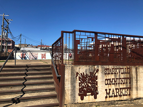 A downtown lot includes a concrete slab and “Starkville Community Market” signage