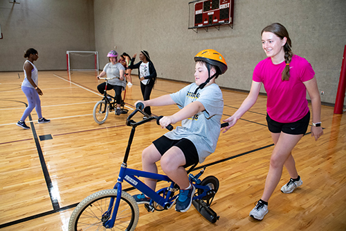 A boy rides a bike as helpers watch close-by