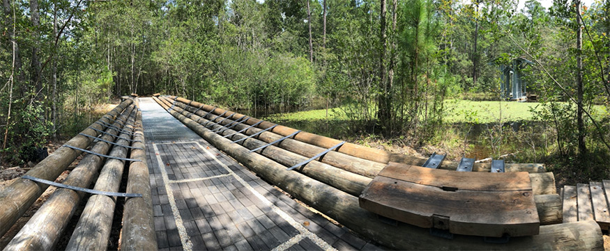 A long bridge framed by logs is shown surrounded by trees
