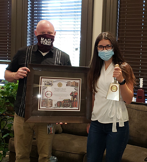 Mississippi State Dean of Students Thomas Bourgeois holds a framed award as Reagan Scott holds a cowbell. 