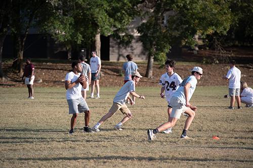 A quarterback drops back for a pass as two receivers run down the practice field.