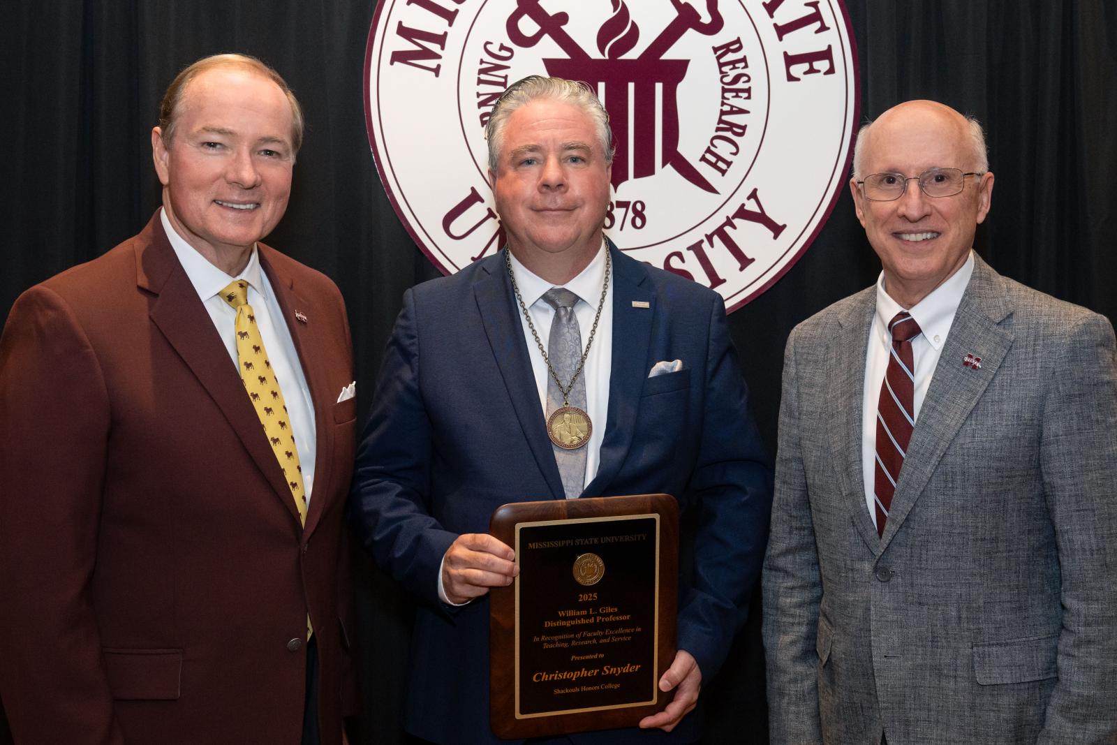 three men pose with award in front of MSU seal