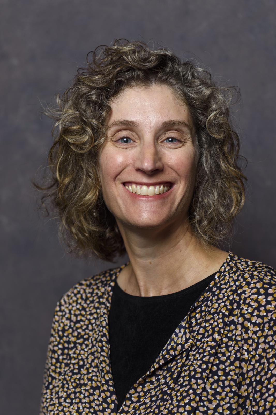 headshot of woman with curly hair on a grey background