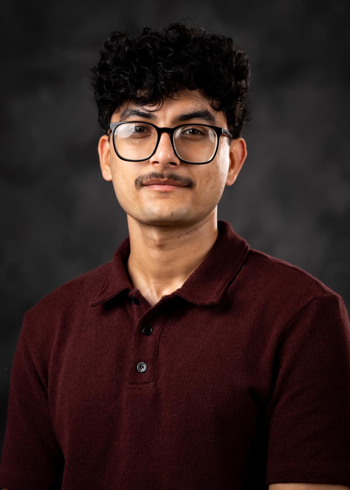 Headshot of Swarup Bhattarai in a maroon polo on a black background