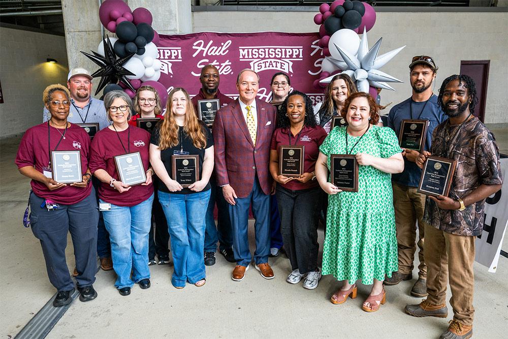 A dozen MSU staff are being recognized with 2026 Zacharias Distinguished Staff Awards for exemplary work in their roles at the university. Being congratulated by MSU President Mark E. Keenum, center, are, front row, from left, Donna Reese, MaryAnn Latham, Tracy Wilcox, (Keenum), Rhonda Hannah, Delaney Foster and Brentson Hall; back row, from left, Mark Hall, Paige White, Alexis Hamilton, Brittany Adams, Ashlee Reed and Zack Ivy.