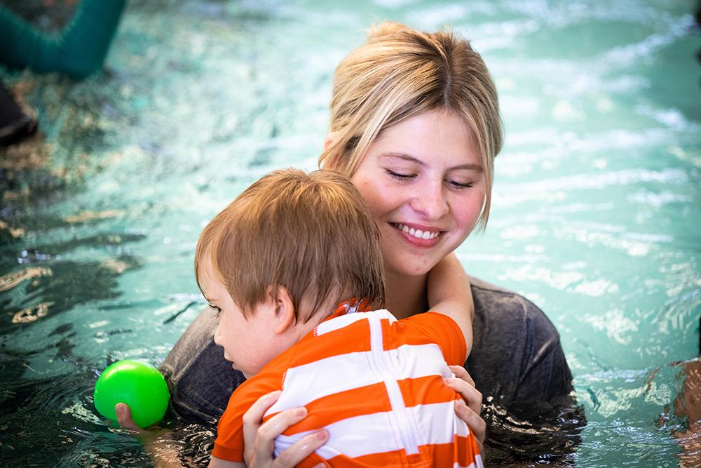 A Mississippi State swim instructor holds a child in a pool.