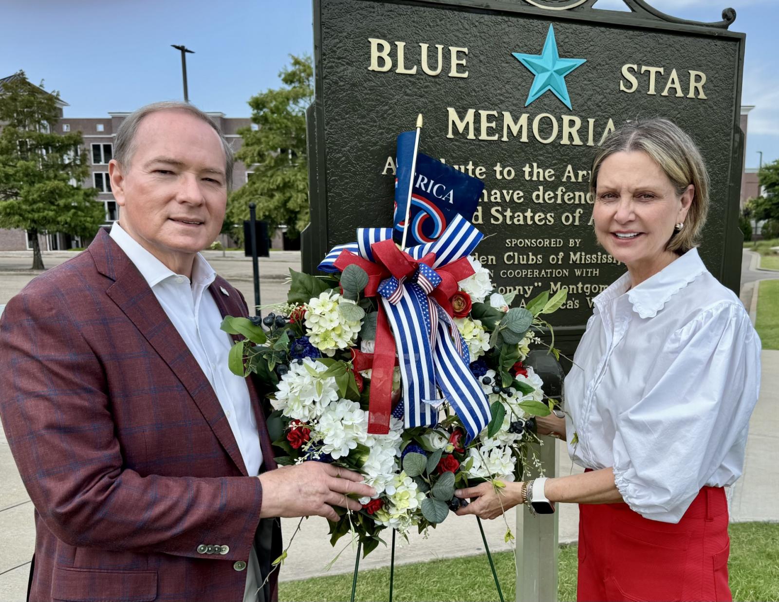 photo of MSU president Mark Keenum and First Lady Rhonda Keenum with flowers in front of the Blue Star Memorial at MSU