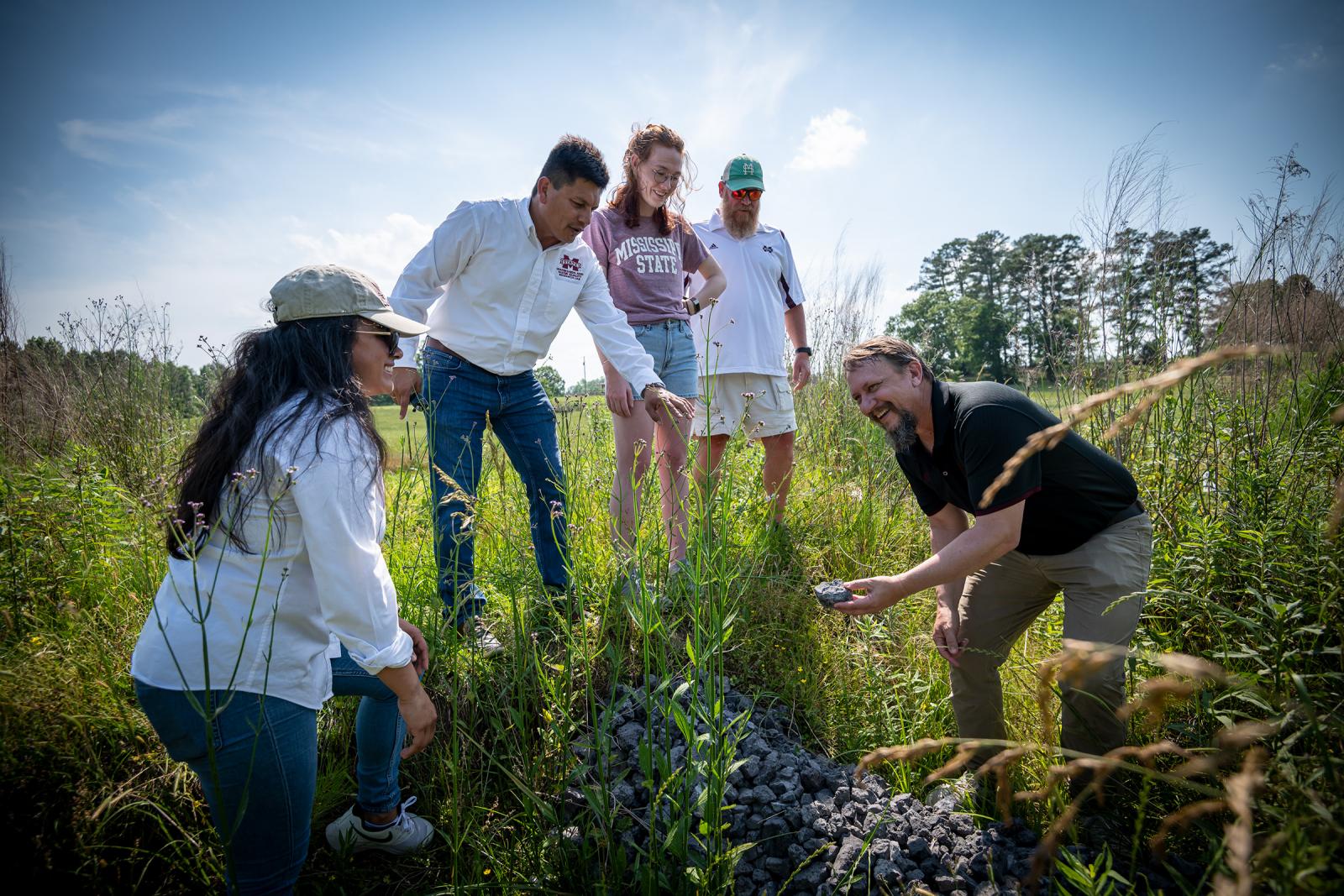 Two men standing in a field showing a piece of slag to students.