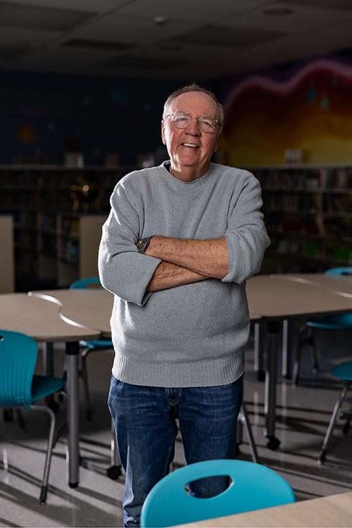 A portrait photo of James Patterson taken while he stands in a classroom.