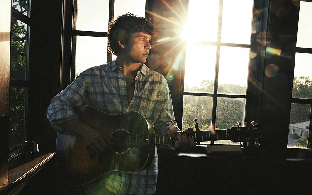 A press image of Vincent Mason playing guitar in a sun room.
