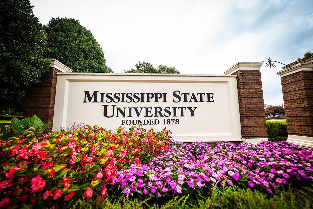 A campus entrance sign at Mississippi State University with flowers in the foregrounds