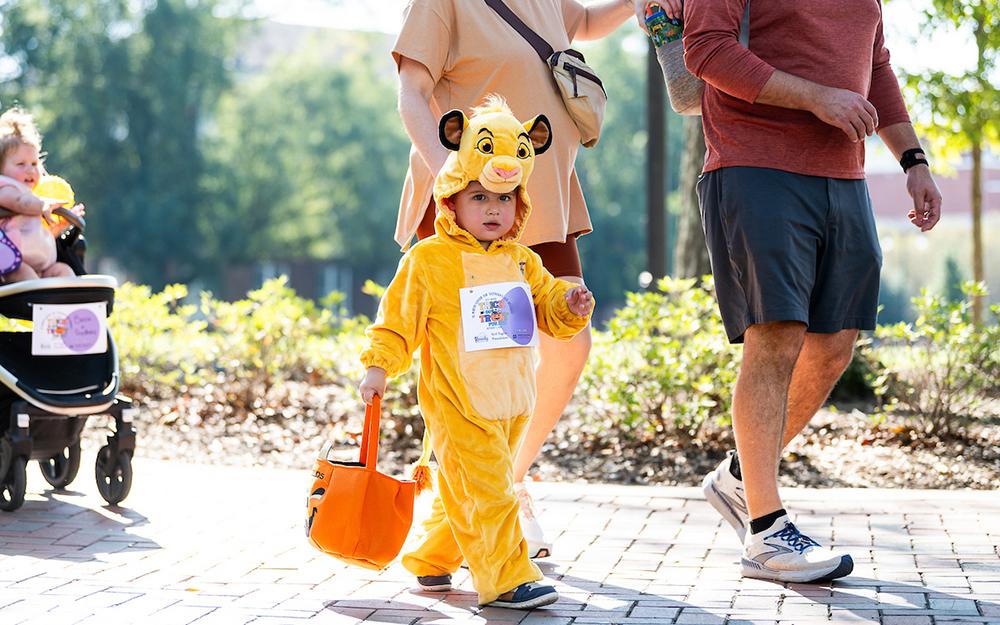 A child dressed in a Halloween costume walks on campus with its parents.