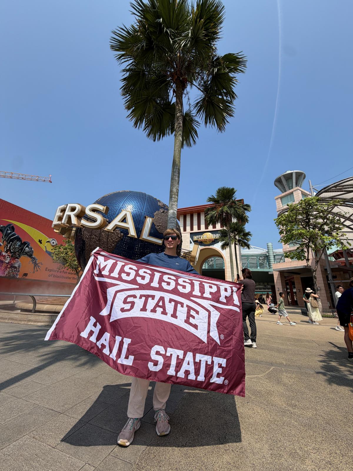 Apollo Stafford standing in Singapore with an MSU flag.